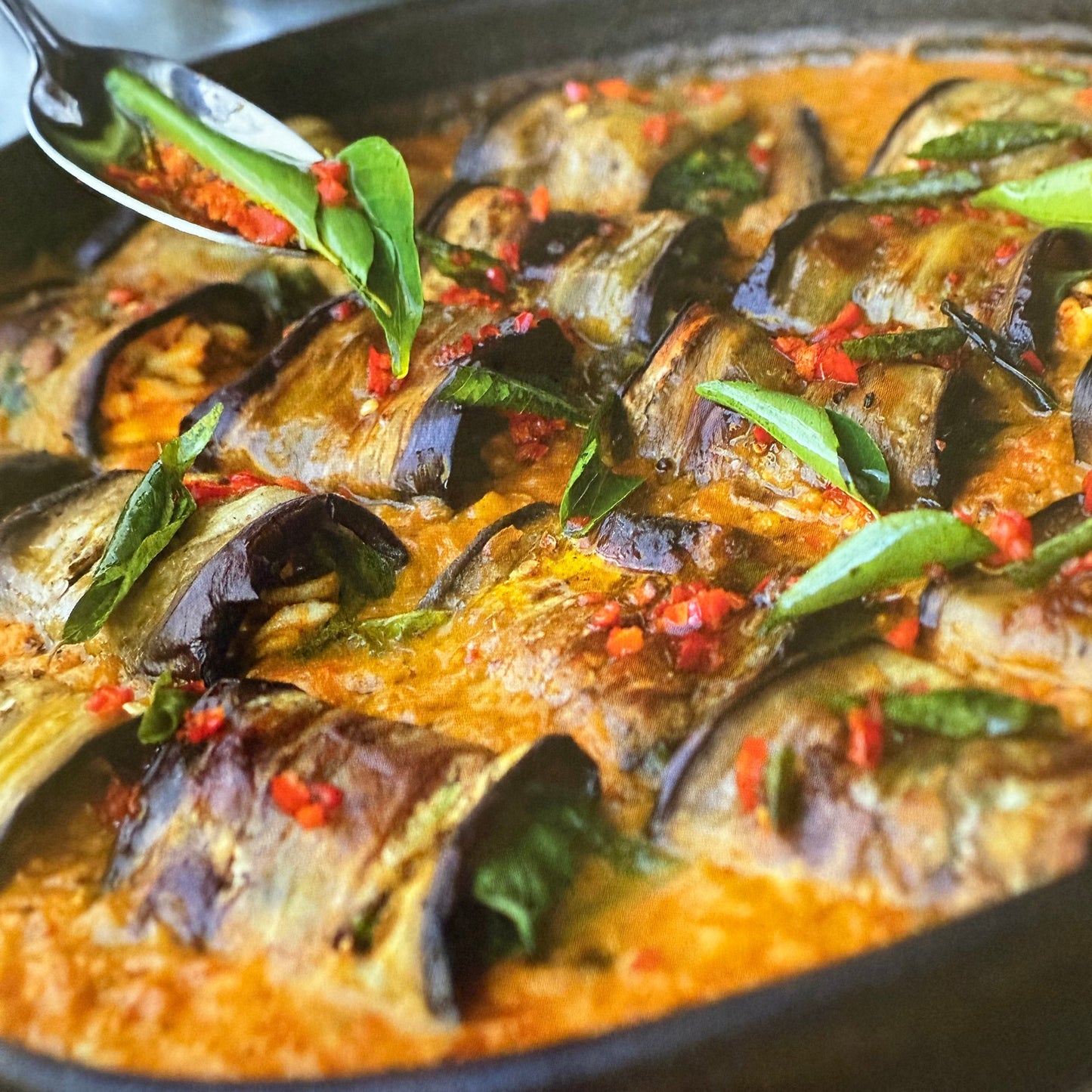 Steamed fish dish with green herbs and red spices on a black plate