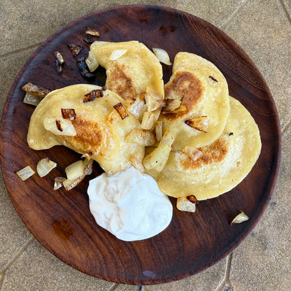 Three pierogies on a wooden plate with a dollop of sour cream on a stone surface.